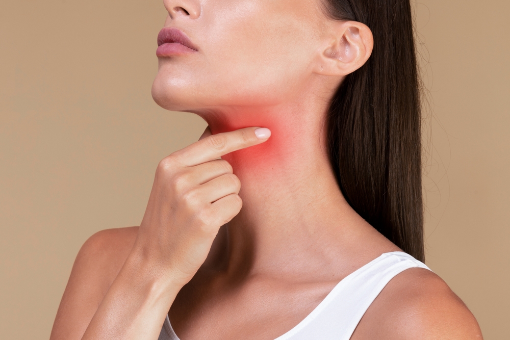 Woman pointing to red inflamed area on her neck indicating thyroid problems